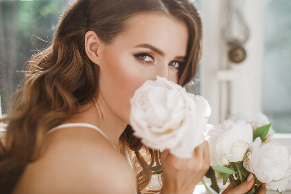 adorable young bride holds a bouuqet of peonies siting on the wi