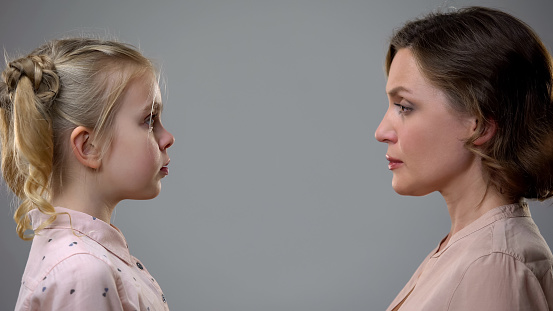 strict mother looking scared daughter on grey background, discipline upbringing